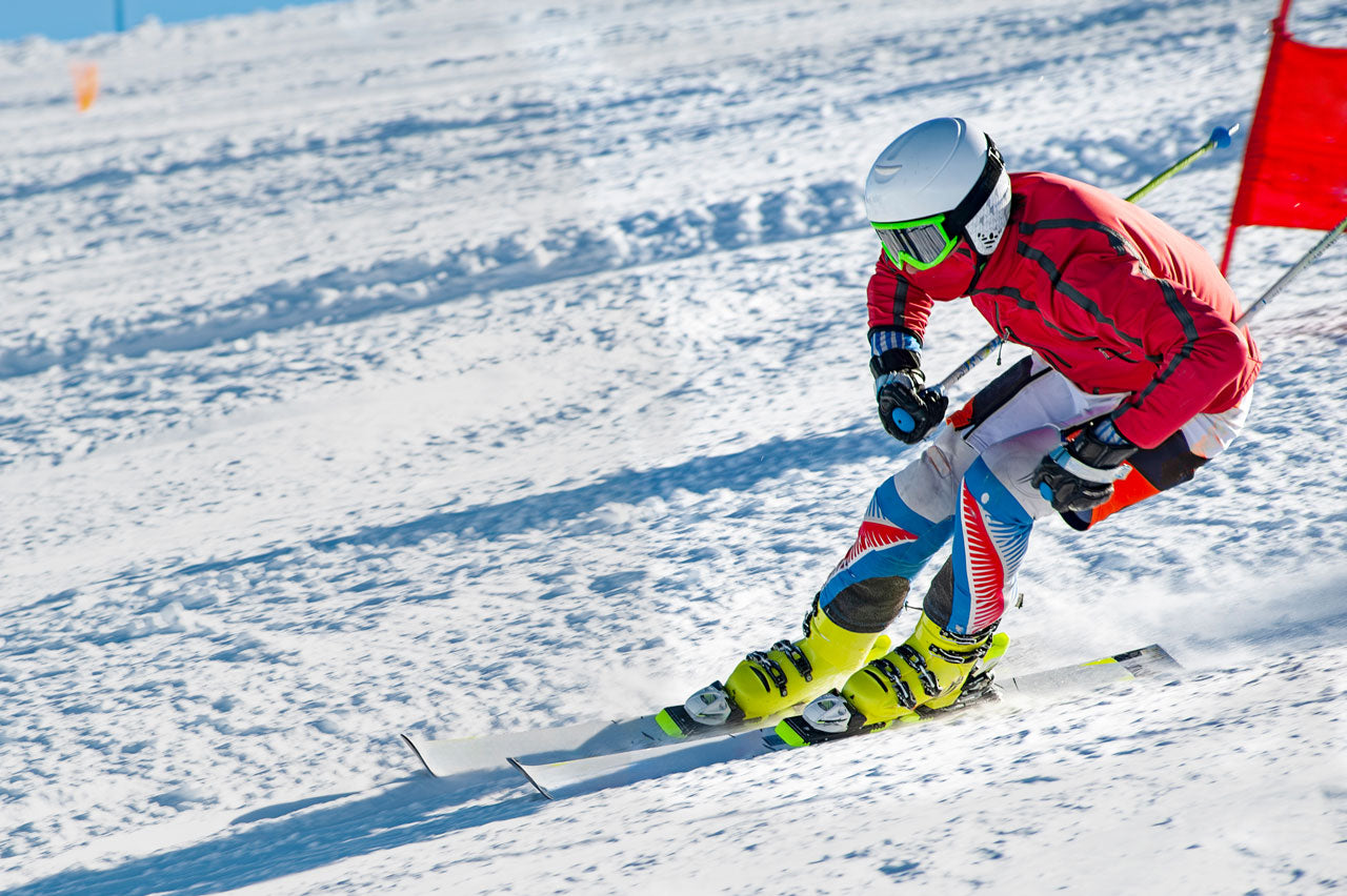 Skier in red jacket and colorful pants skiing downhill with a red flag on a snowy slope