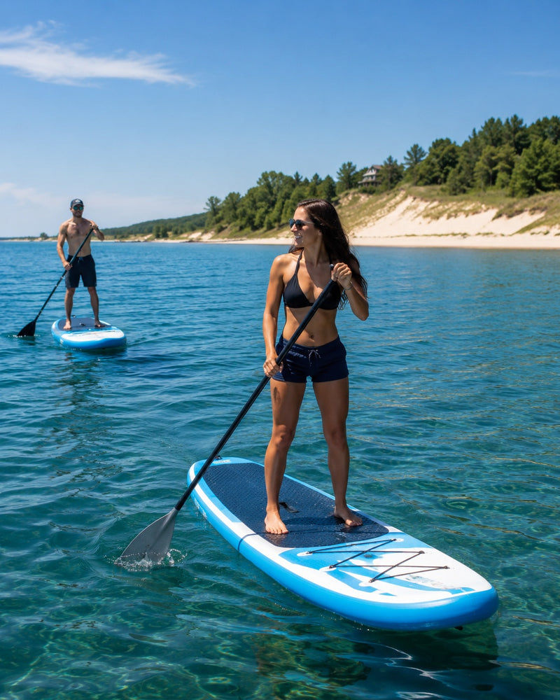 Woman paddleboarding on calm water along the Lake Michigan shoreline at sunset.